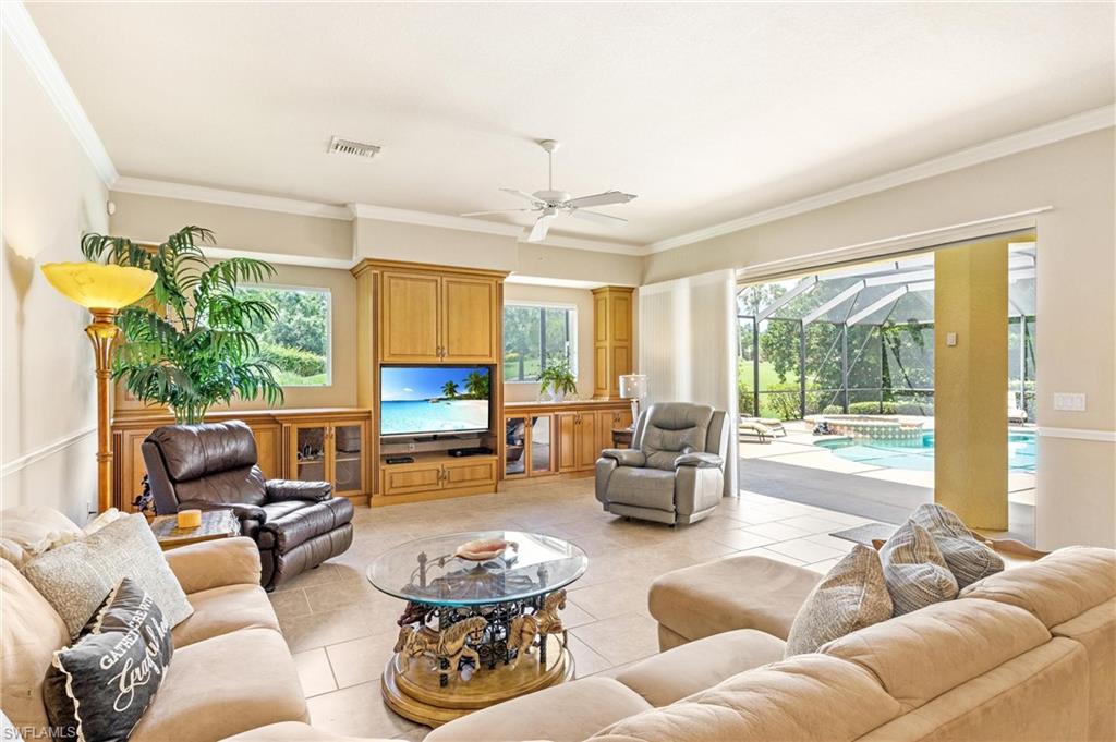 Spacious living area featuring tile flooring, crown molding, a ceiling fan, and built-in wood cabinetry with display storage