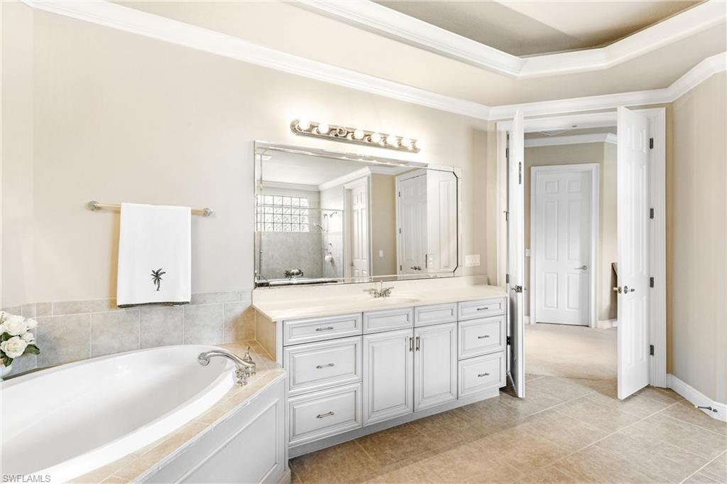 Spacious bathroom featuring a white soaking tub, an extensive white vanity with a light-colored countertop, and a large mirror with decorative lighting