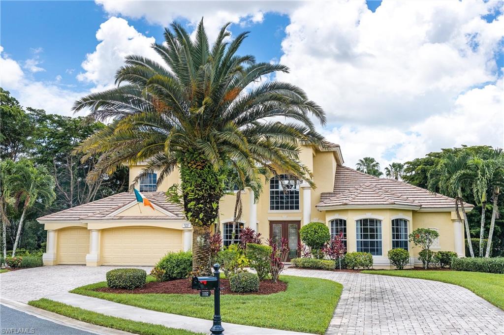 Stucco exterior with a tile roof, an arched entry, a prominent two-story window, a paver driveway, and mature landscaping