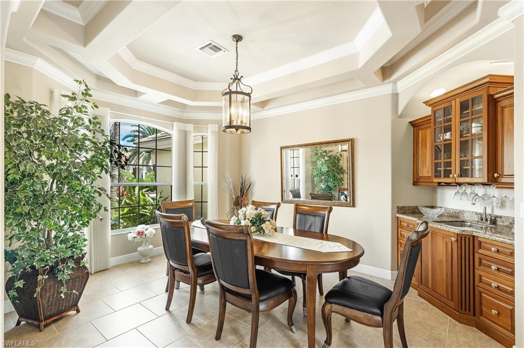 Dining area featuring a coffered ceiling with crown molding, a built-in wet bar with wood cabinetry and a stone countertop, a bay window, and tile flooring