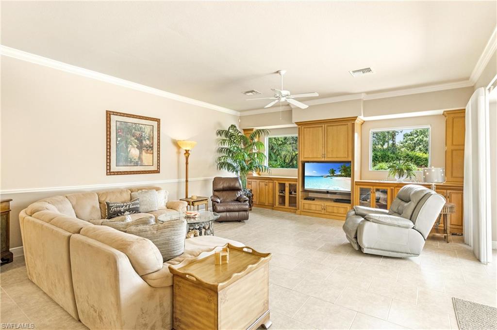 Spacious living area featuring light-toned tile flooring, extensive built-in wooden cabinetry with display shelving, and multiple windows providing natural light