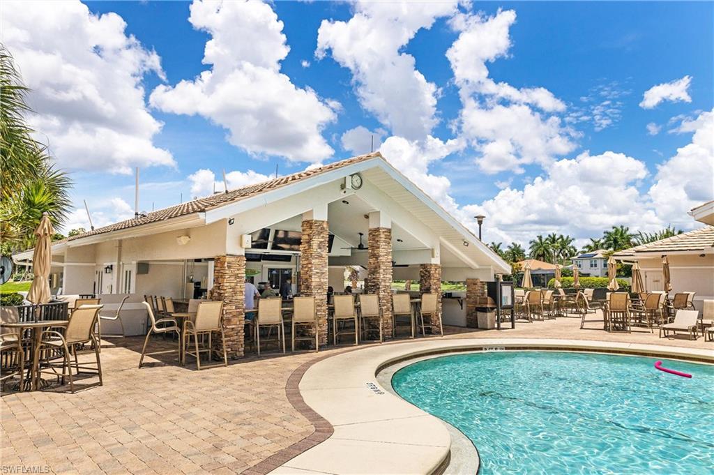 Expansive outdoor amenity area featuring a curvilinear swimming pool, a covered pavilion with a built-in bar, and extensive paver decking