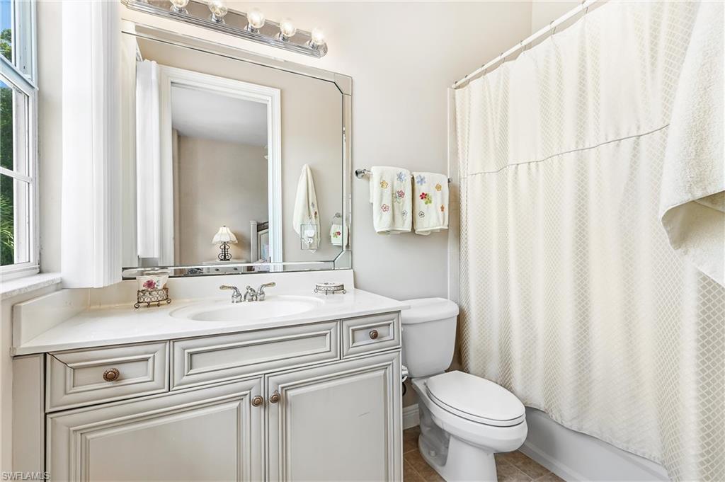 En-suite Bathroom featuring a single basin vanity with a light-colored countertop, an ornate framed mirror, and a shower/tub combination with a white curtain