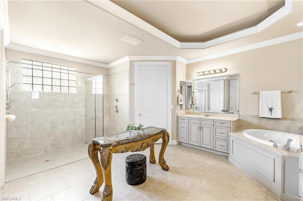 Neutral-toned bathroom featuring a spacious glass-enclosed shower with tile walls and a glass block window, a built-in soaking tub with paneled surround, and a dual-sink vanity with light-colored cabinetry and a large mirror
