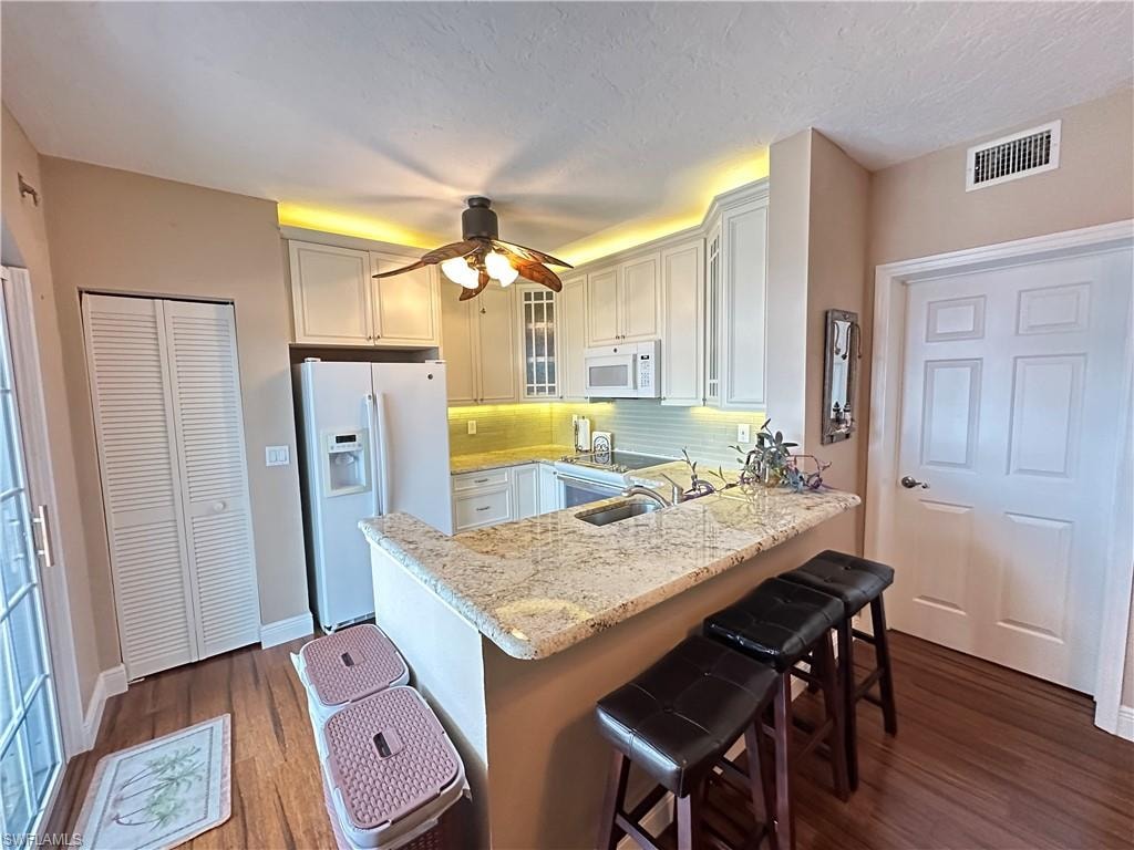 Kitchen featuring wood-finish flooring, light-toned cabinetry, stainless steel sink, granite countertops, and a full suite of white appliances