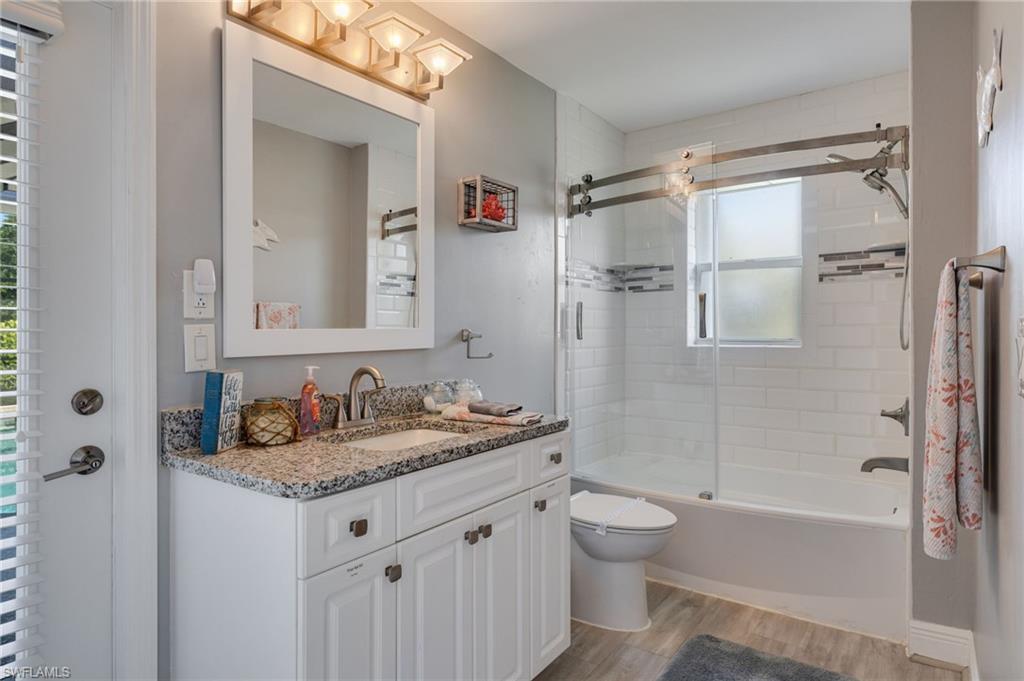 Bathroom featuring a vanity with granite-style countertop and undermount sink, a white framed mirror, and a shower-tub combination with sliding glass doors
