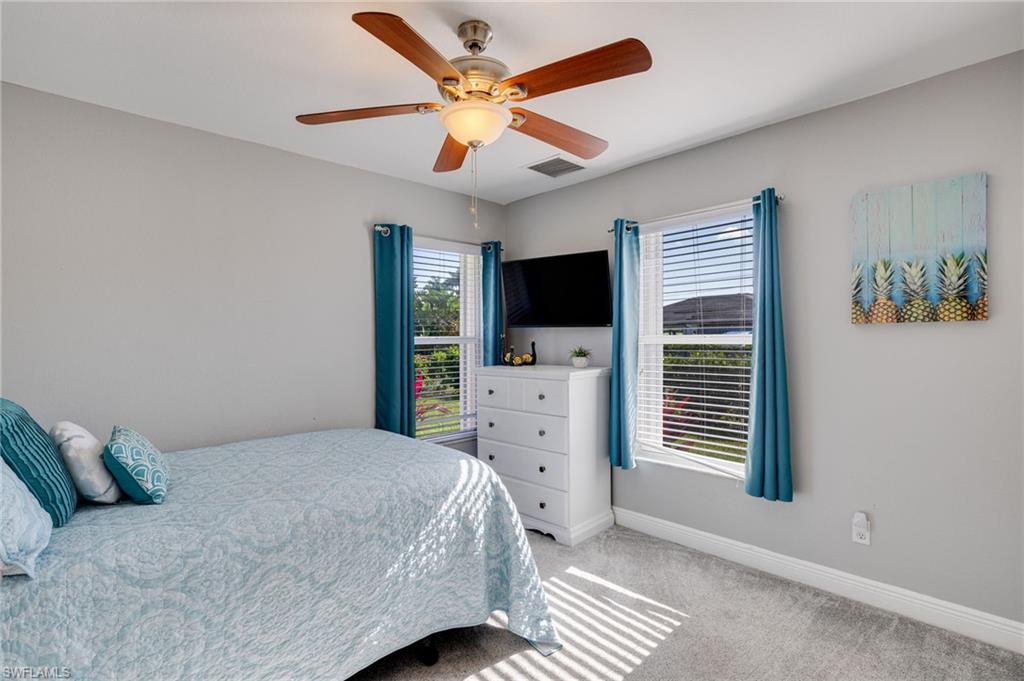 Bedroom featuring a ceiling fan with integrated lighting, two windows with blinds and blue curtains, light grey wall paint, and grey carpet flooring