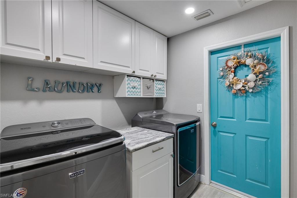 Laundry area featuring white shaker-style cabinetry, a built-in countertop, a top-load washing machine, a front-load dryer, and a vibrant turquoise paneled door