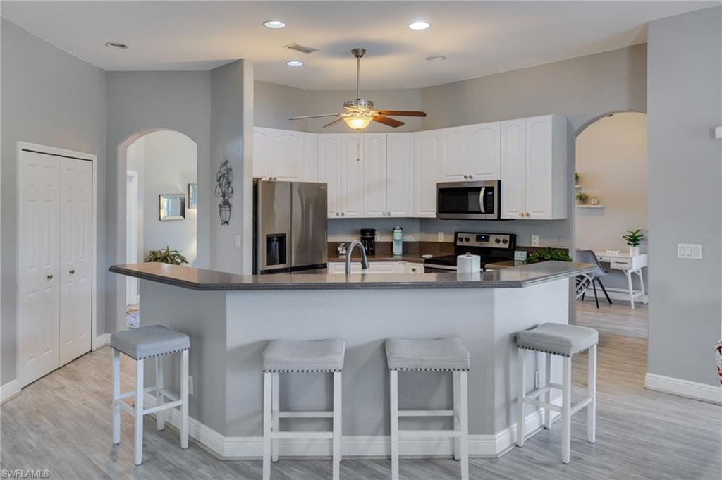 Kitchen featuring white cabinetry, stainless steel appliances, an integrated breakfast bar, wood-finish flooring, and recessed lighting