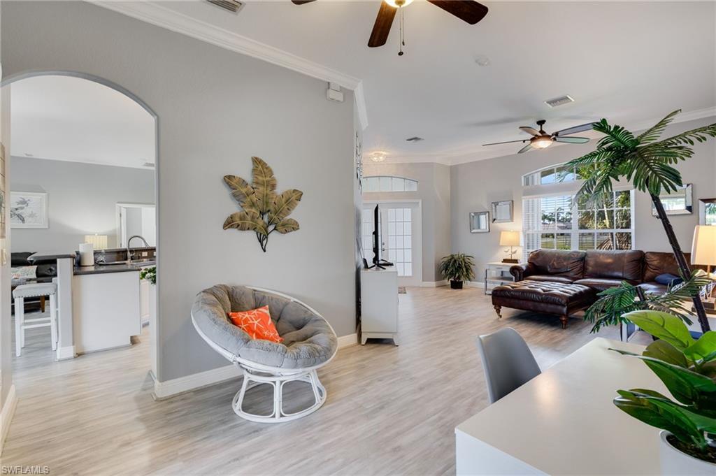 Open-concept living space featuring light wood-finish flooring, an arched doorway, crown molding, and ceiling fans
