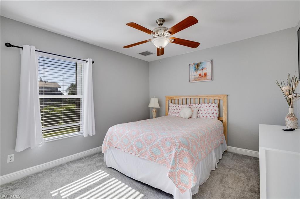 Bedroom featuring light gray wall paint, gray carpeting, a window with blinds and white curtains, a ceiling fan with light, and white baseboards