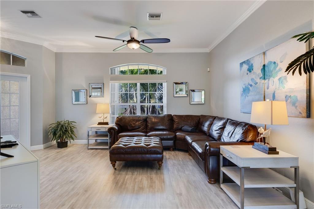 Spacious living area featuring wood-finish flooring, crown molding, and a ceiling fan with integrated lighting