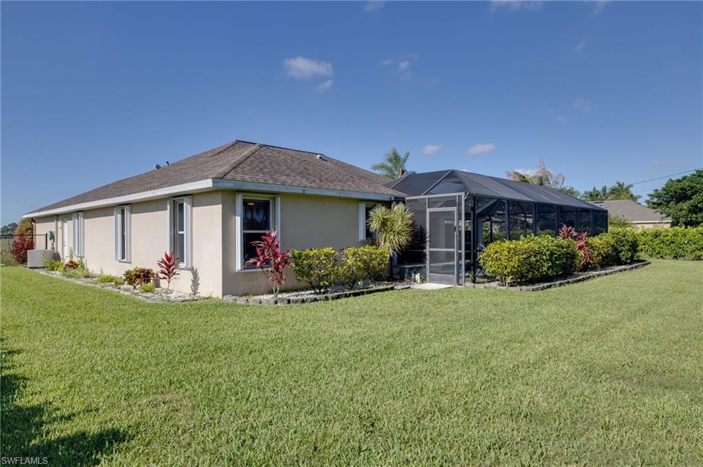 Expansive lawn area featuring a stucco exterior, a screened enclosure, mature landscaping, and a well-defined planting bed border