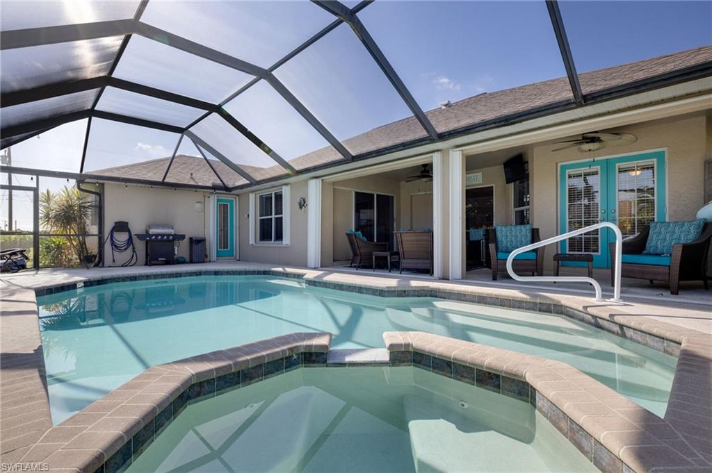 Screen-enclosed pool area featuring a rectangular pool with integrated spa, a paved deck, an exterior patio with ceiling fans, and direct access to the interior via double glass doors