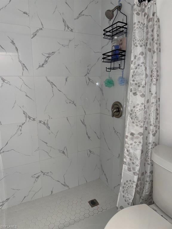 Shower enclosure featuring large format white tile walls with gray veining and a hexagonal mosaic tile floor