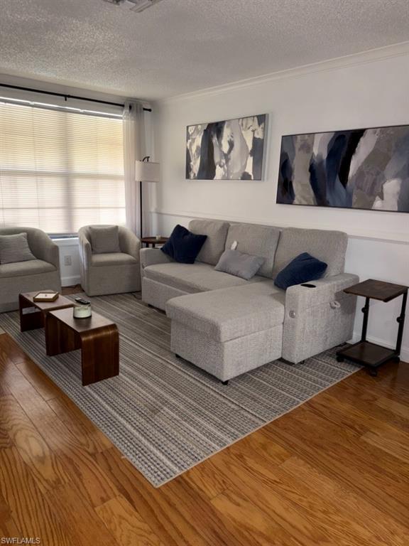 Living area featuring wood-finish flooring, white wall molding, and a large window with blinds