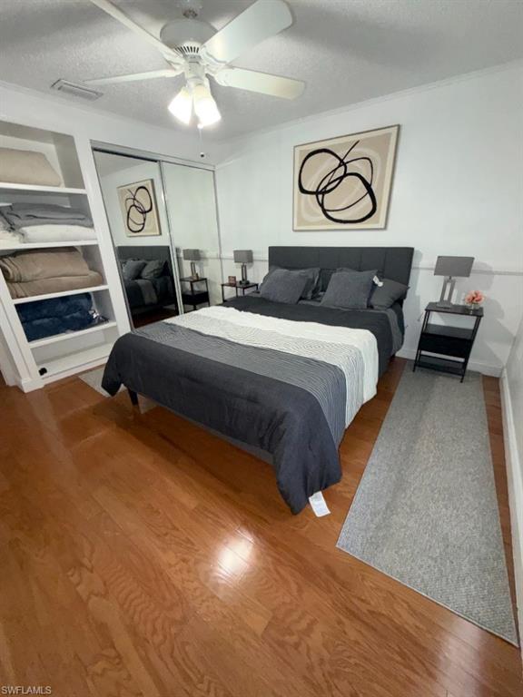 Bedroom featuring wood-finish flooring, built-in shelving, mirrored closet doors, a white ceiling fan with integrated lighting, and crown molding