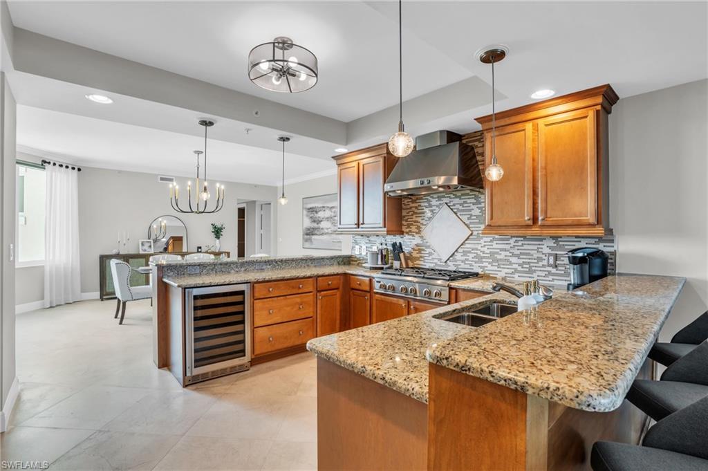 Kitchen with decorative light fixtures, wall chimney range hood, beverage cooler, kitchen peninsula, and backsplash