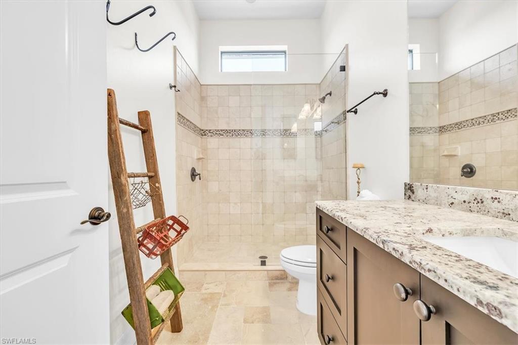 Spacious bathroom featuring a glass-enclosed shower with tile surround and decorative accent band, a single vanity with stone countertop, and integrated sink