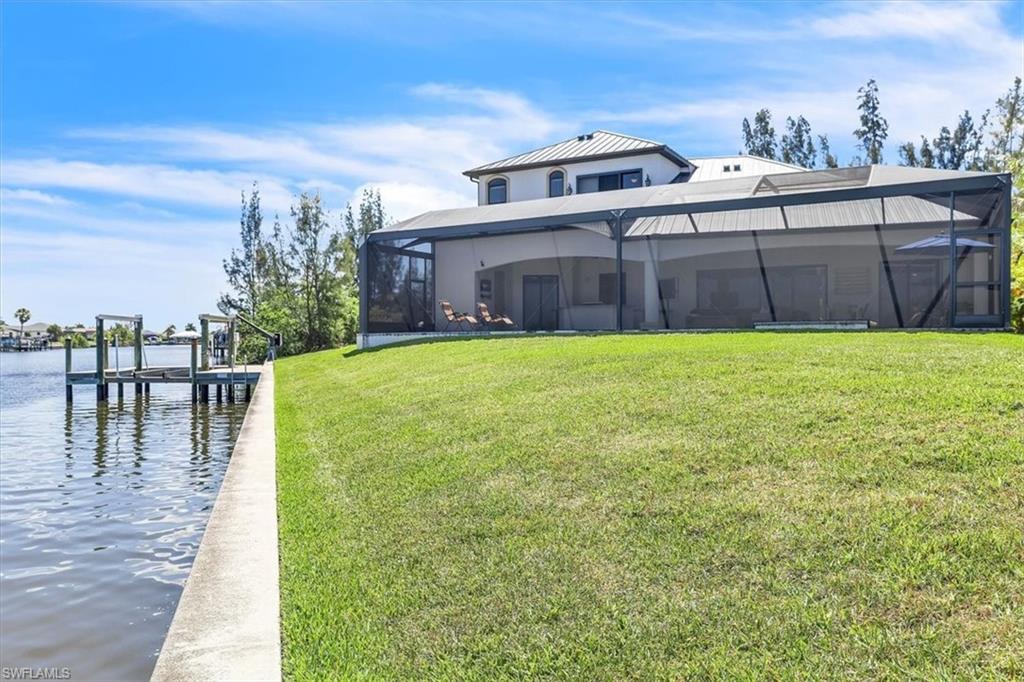 Waterfront property featuring a private boat dock, concrete seawall, expansive green lawn, and a screened-in rear patio