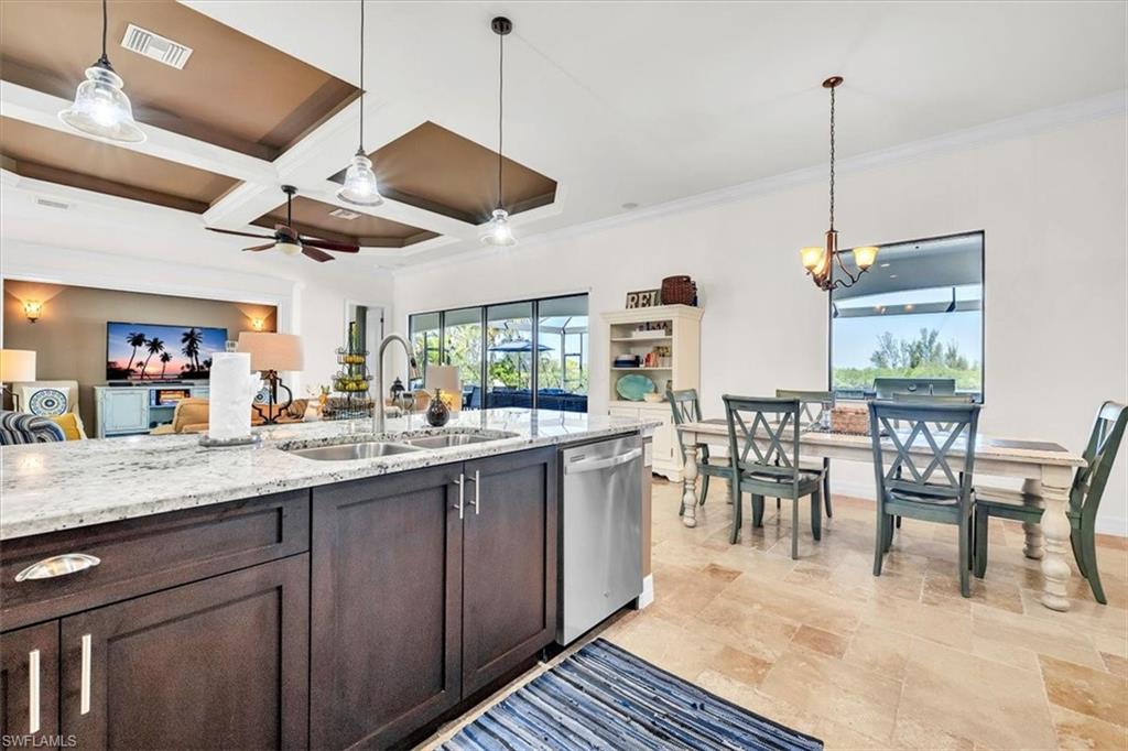 Open-concept kitchen and dining area featuring wood-finish cabinetry, a large kitchen island with a double basin sink, stainless steel dishwasher, and light stone countertops
