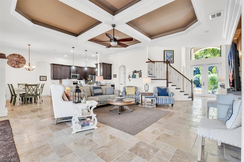 Open-concept living space featuring coffered ceilings, large format tile flooring, and a grand staircase with dark wood treads and white risers