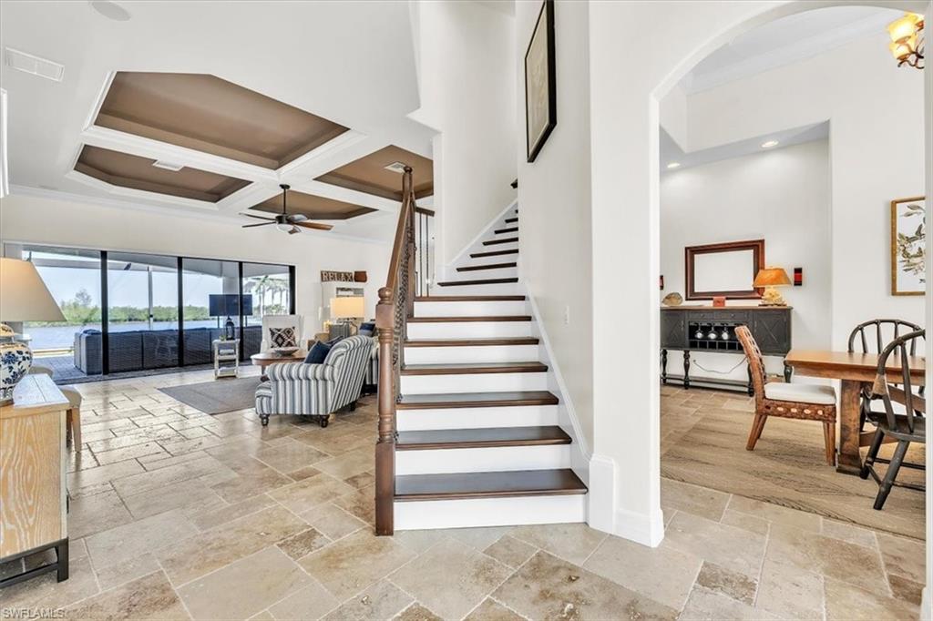 Open-concept living area with coffered ceilings, tile flooring, and a staircase featuring wood treads and a wood handrail