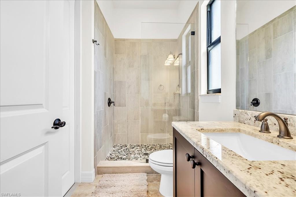 Bathroom featuring a glass-enclosed shower with pebble flooring and tiled walls, a dark wood-finish vanity with a granite countertop, an undermount sink, and a bronze-finish faucet