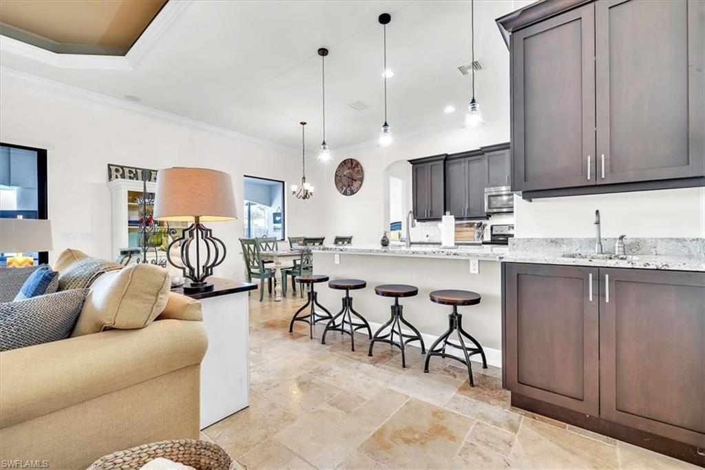 Open-concept living space featuring light-toned tile flooring, tray ceiling, dark wood cabinetry, light-toned countertops, and a kitchen island with pendant lighting