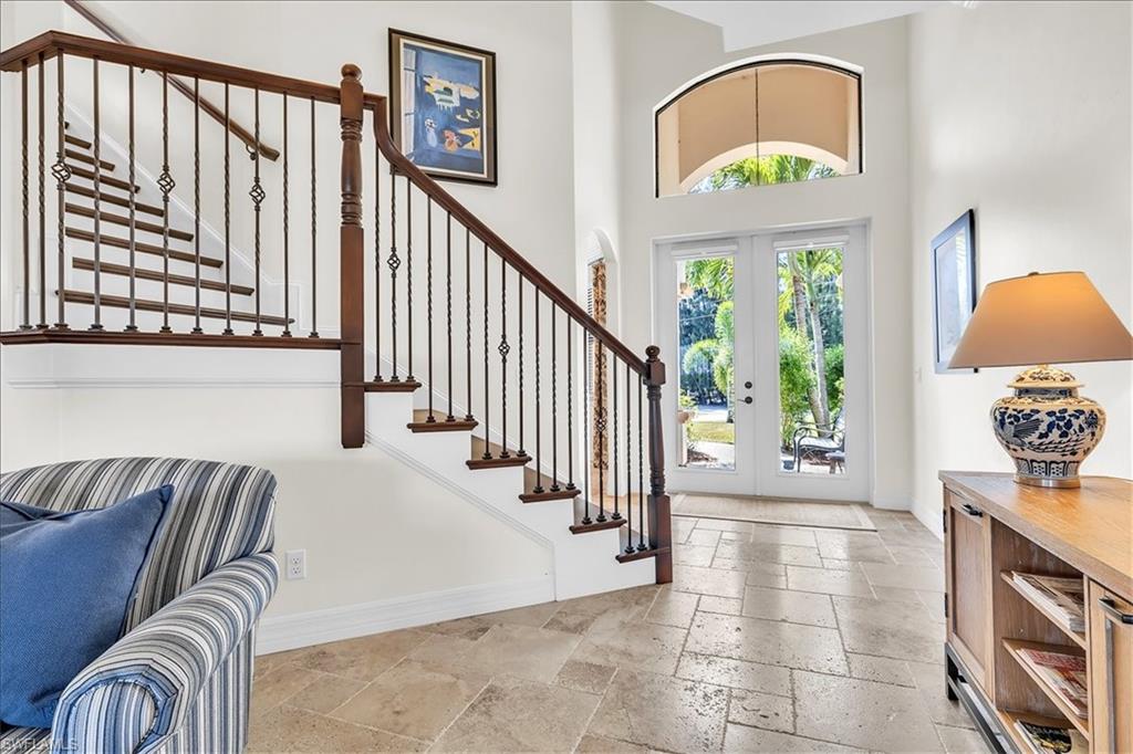 Two-story entry foyer featuring a grand staircase with wrought iron balusters and wood handrails, double-door entry with an arched transom, and stone tile flooring