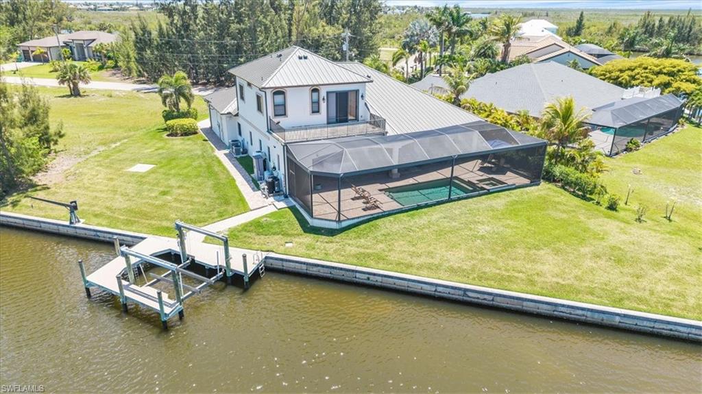 Waterfront property featuring a private boat dock with lift, screened pool enclosure, expansive pool deck, upper-level balcony, and mature landscaping