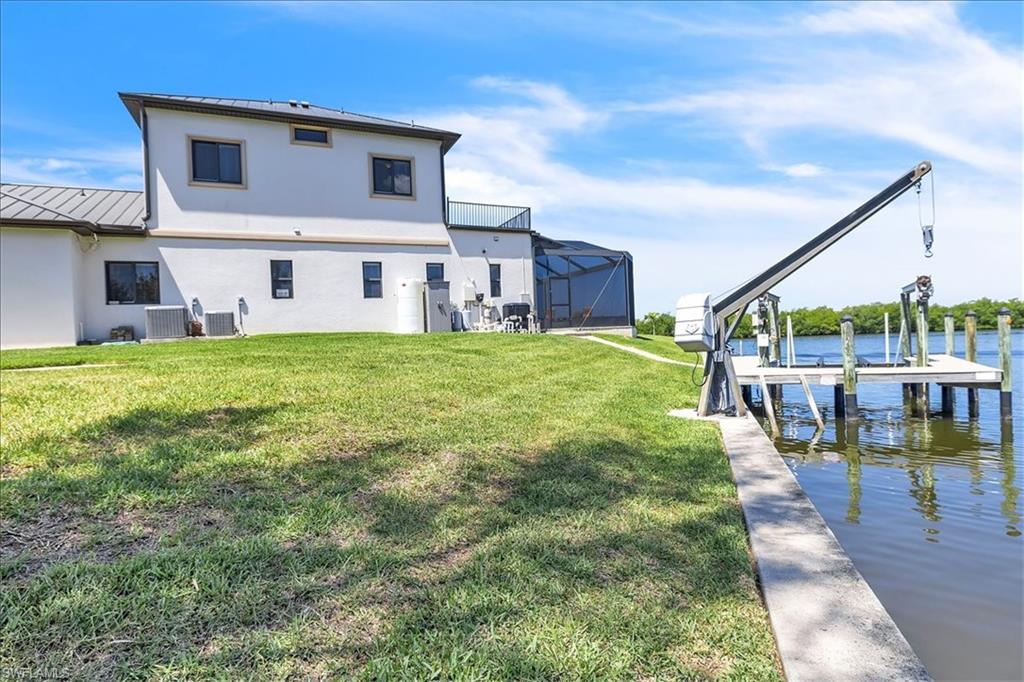 Waterfront property featuring a private dock with a boat lift, a screened lanai, and a manicured lawn
