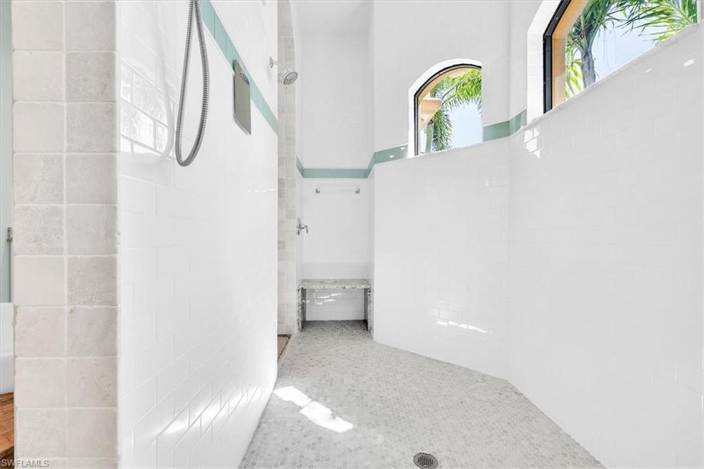 Expansive shower with white subway tile walls, light mosaic floor tile, built-in bench, and arched transom windows
