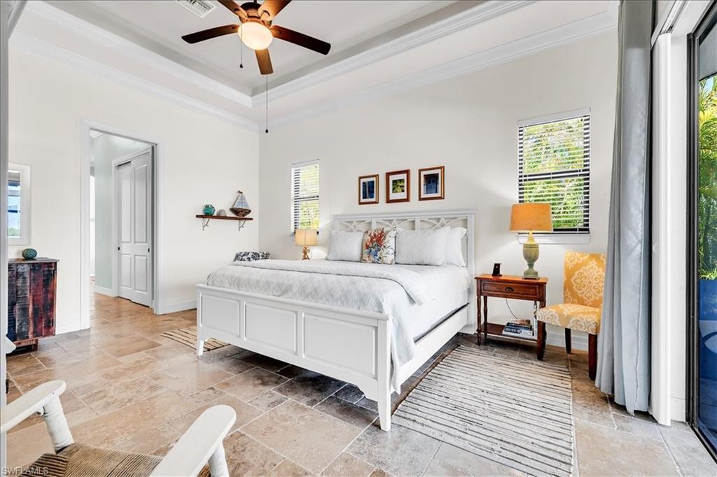 Spacious bedroom featuring large format tile flooring, crown molding, and a tray ceiling with a ceiling fan