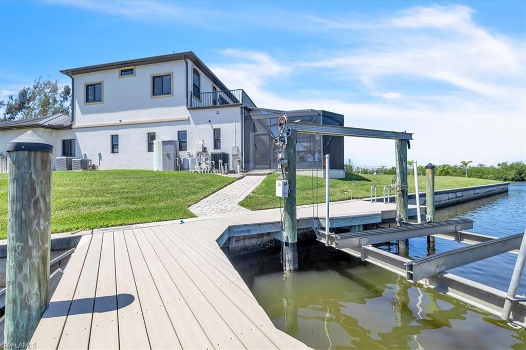 Waterfront property featuring a private boat dock with lift, paver walkway, and a manicured lawn