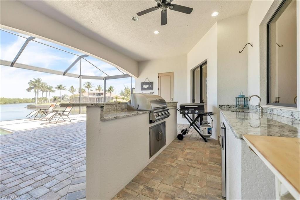 Expansive screened patio featuring paver flooring, a built-in outdoor kitchen with a gas grill and stone-finish countertops, and a ceiling fan