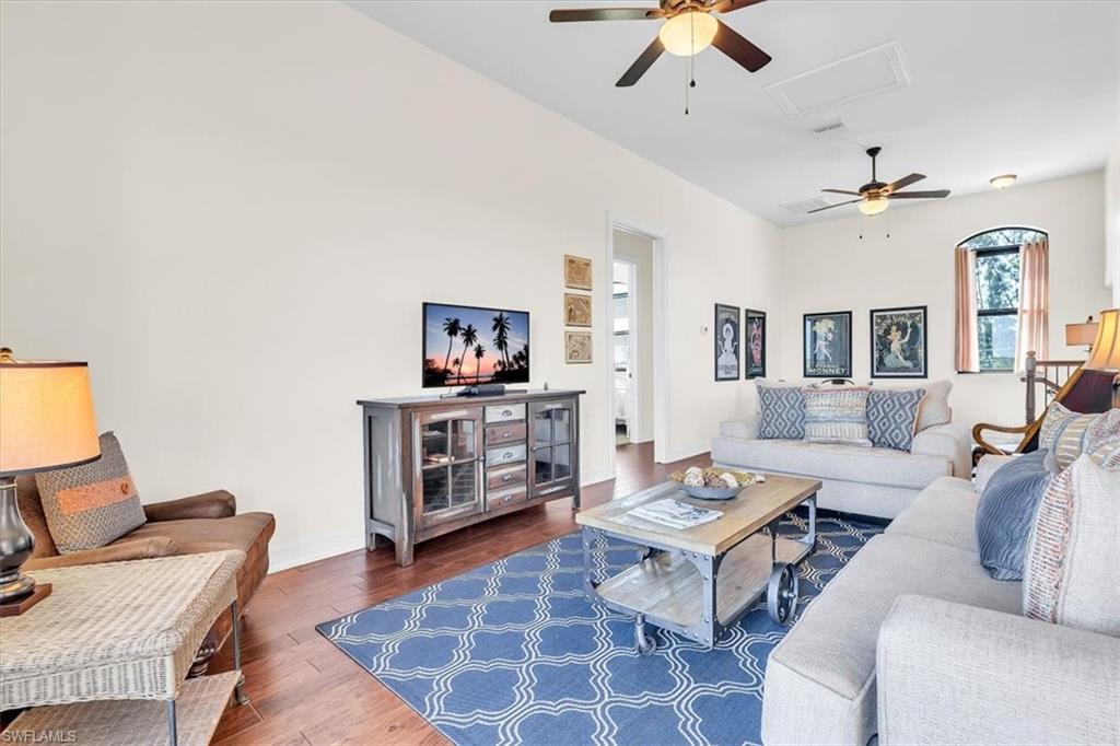 Spacious living area featuring high vaulted ceilings, multiple ceiling fans with integrated lighting, wood-finish flooring, a decorative arched window, and a built-in media console