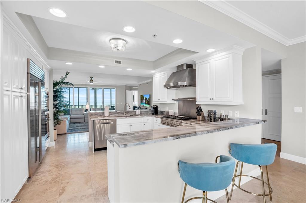 Kitchen with white cabinetry, kitchen peninsula, wall chimney range hood, and stainless steel appliances