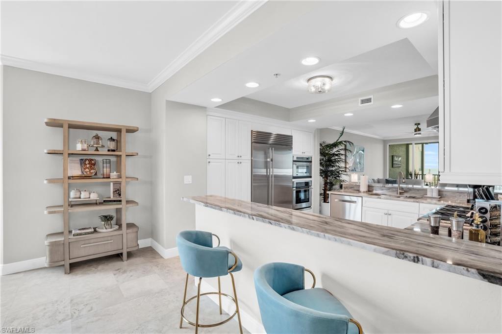 Kitchen featuring stainless steel appliances, kitchen peninsula, light tile patterned floors, white cabinetry, and ornamental molding