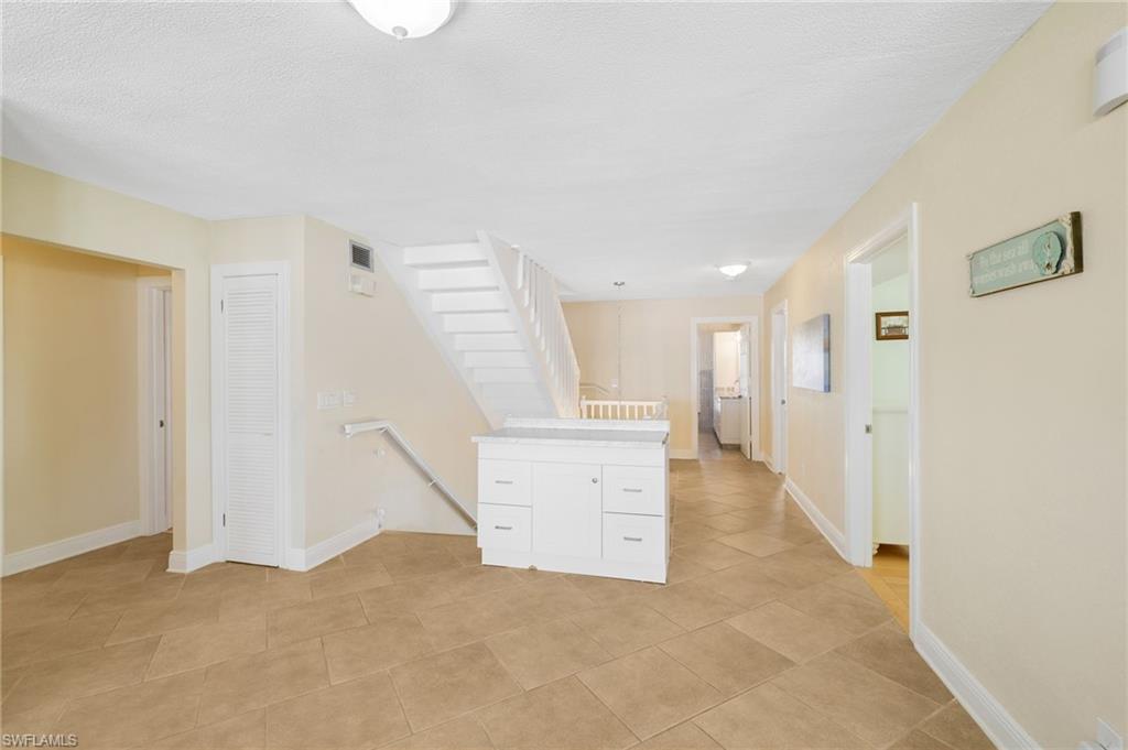 Interior living area featuring large format tile flooring, a white staircase with a matching railing, and a built-in island with cabinet storage - Virtually Edited Image