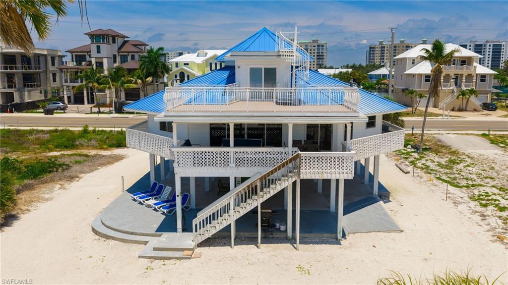 Elevated coastal residence featuring a vibrant blue metal roof, multiple levels of outdoor decking, a spiral staircase, and decorative white railings - Virtually Edited Image