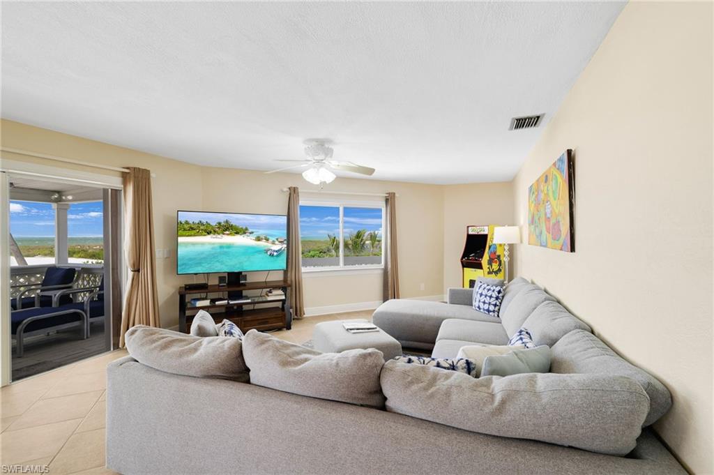 Spacious living area featuring tiled flooring, a ceiling fan, and large windows offering exterior views - Virtually Edited Image