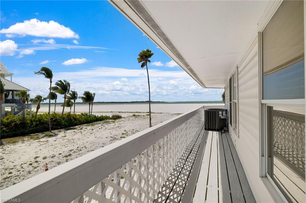 Expansive balcony with white lattice railing and wood-finish flooring, overlooking a sandy landscape and distant body of water - Virtually Edited Image