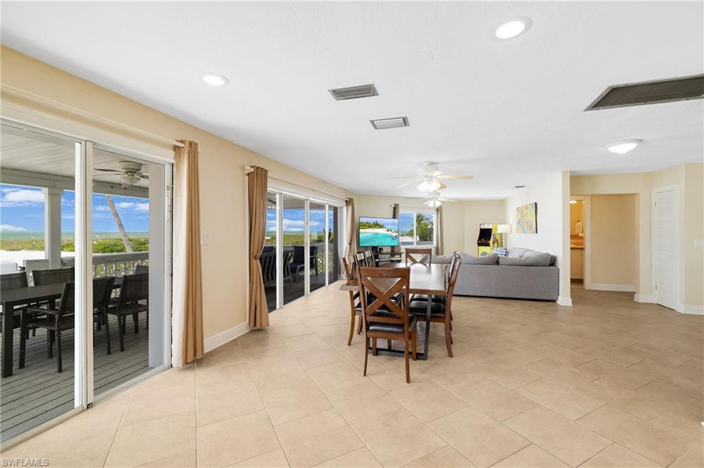 Spacious interior featuring neutral tile flooring, recessed lighting, and expansive sliding glass doors opening to an outdoor deck - Virtually Edited Image