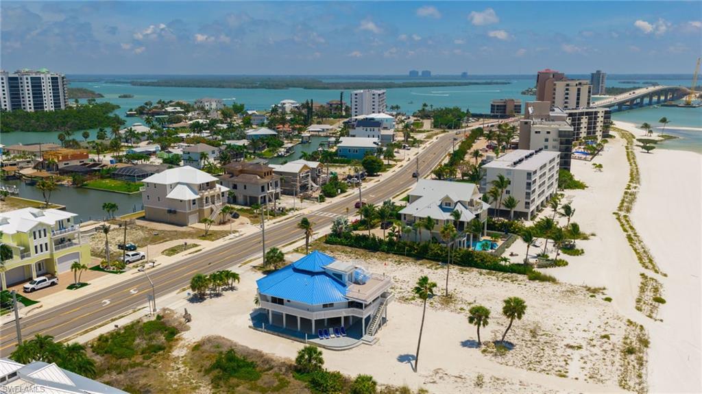 Coastal property featuring a vibrant blue roof, multiple balconies, a raised foundation, and palm trees within a beach and canal-front environment - Virtually Edited Image