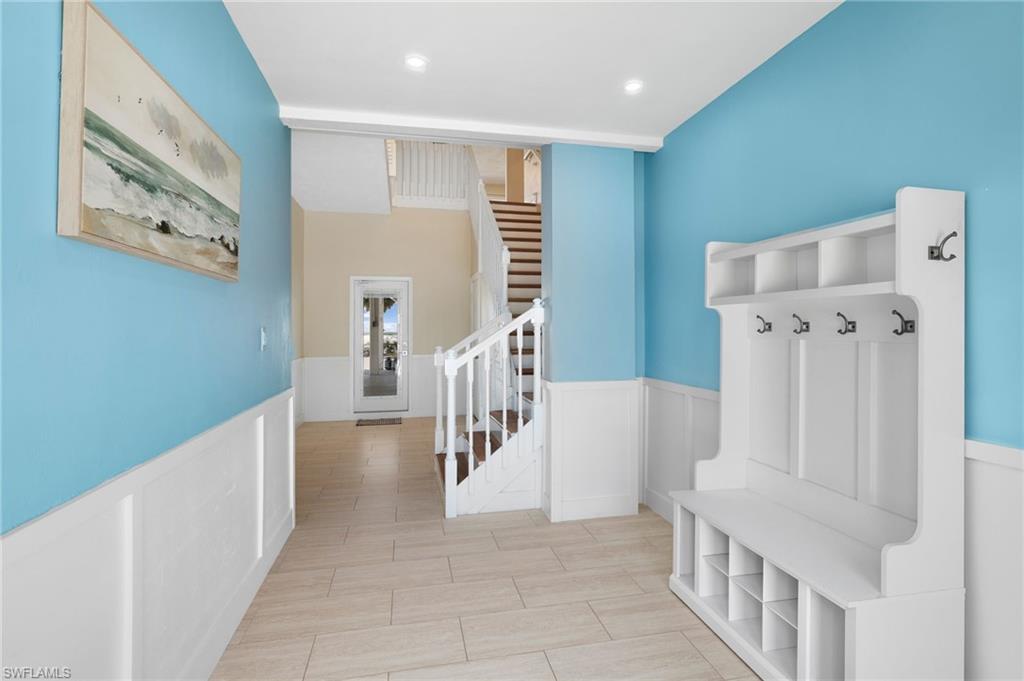 Entryway featuring wood-finish flooring, wainscoting, and a built-in hall tree with storage and hooks - Virtually Edited Image
