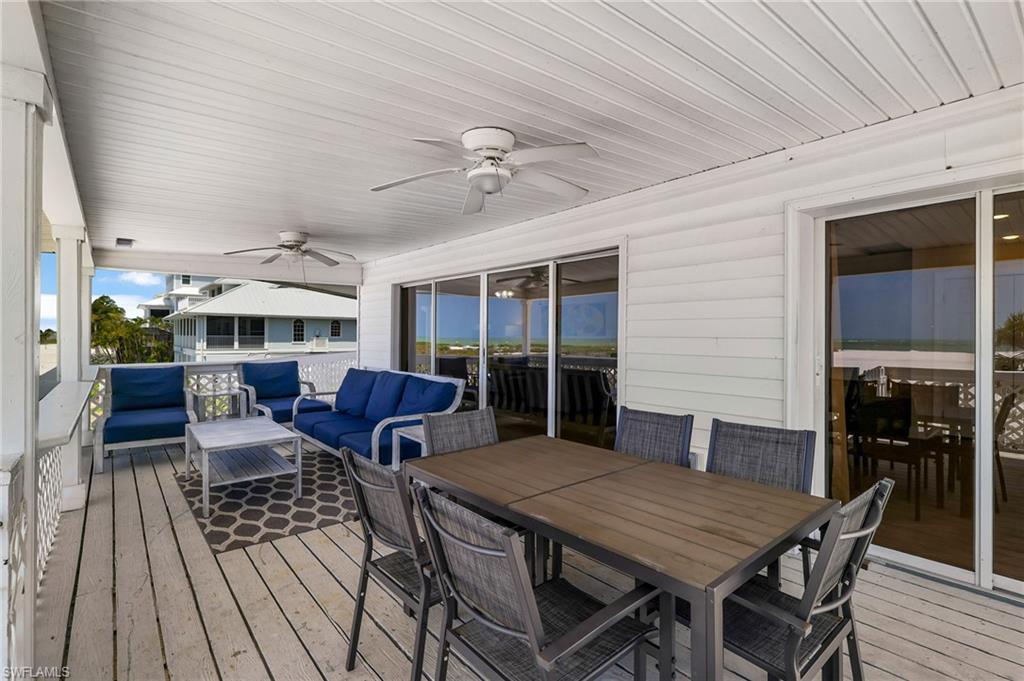 Expansive covered porch featuring a planked ceiling with two ceiling fans, white siding, and a wooden planked floor - Virtually Edited Image