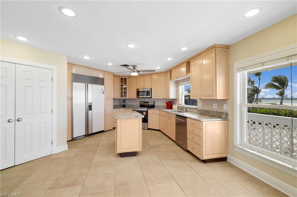 Spacious kitchen featuring light wood cabinetry, stone countertops, stainless steel appliances, and large format tile flooring - Virtually Edited Image
