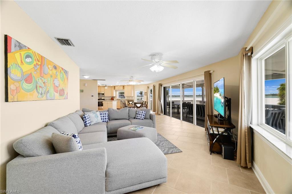 Open-concept living area featuring neutral-toned walls, tile flooring, a ceiling fan, and large windows with water scenery - Virtually Edited Image