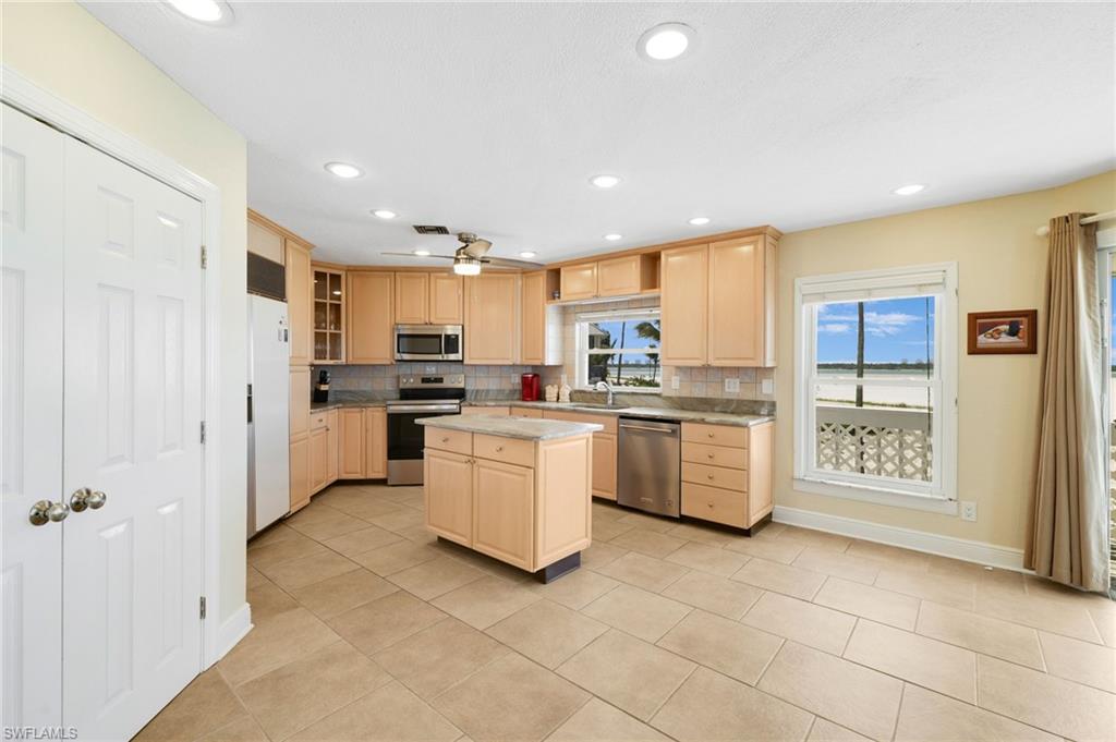 Kitchen featuring light wood-finish cabinetry, stainless steel appliances, a center island with countertop, tile flooring, and recessed lighting - Virtually Edited Image